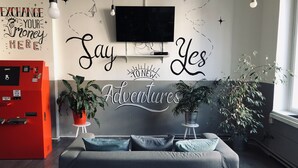 Una sala de estar moderna con un sofá gris, dos plantas en macetas y un televisor montado en la pared.