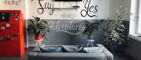 A modern living room with a grey sofa, two potted plants, and a wall-mounted TV.