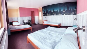 Habitación de hotel con dos camas individuales, un escritorio con silla, una mesita pequeña, un ventilador y un mural de cielo estrellado en la pared.