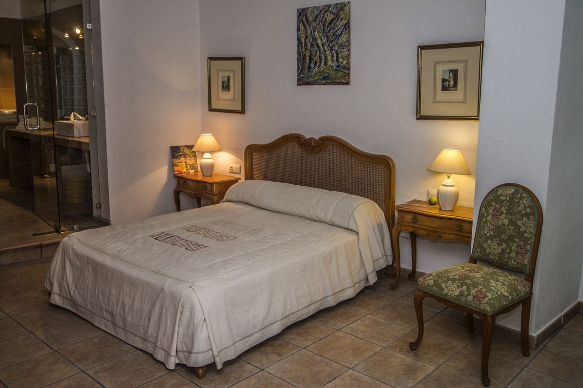 A hotel room with a large bed, two bedside tables with lamps, a chair, and framed pictures on the walls.