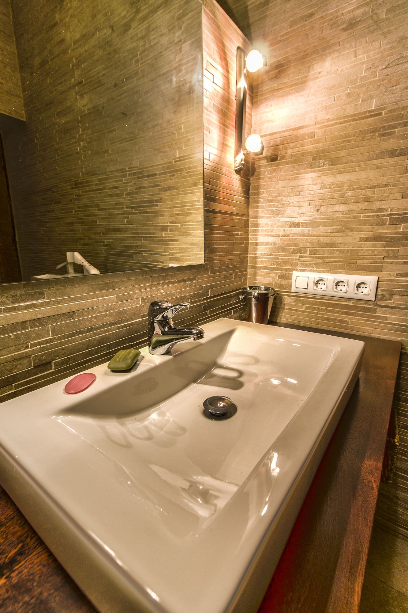 A bathroom with a large sink, a mirror, and a wall-mounted light fixture.