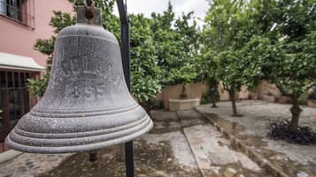 A bell hanging outdoors, likely in a courtyard with a building in the background.