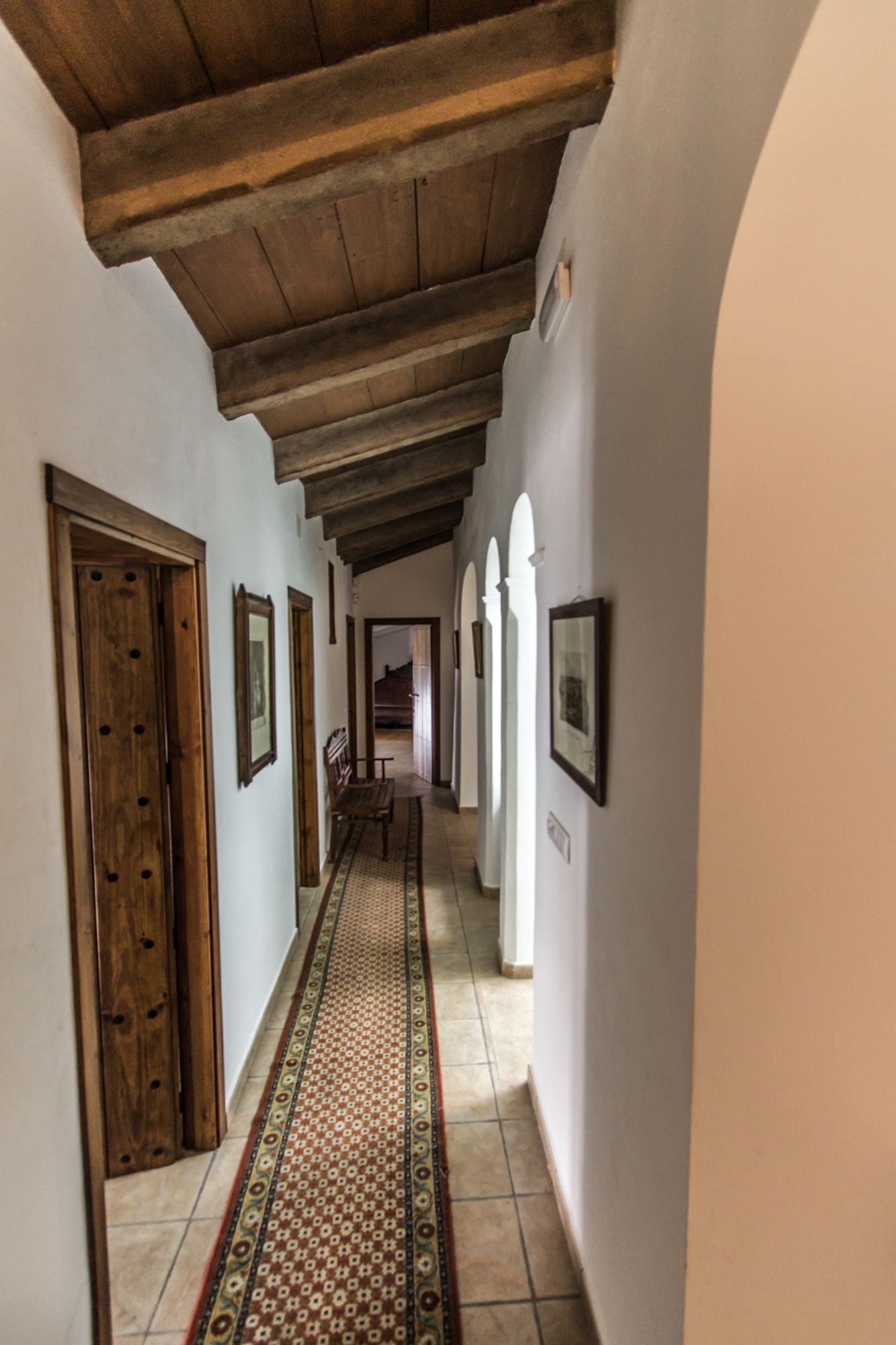 A hallway with wooden doors, patterned rugs, and framed pictures on the walls.
