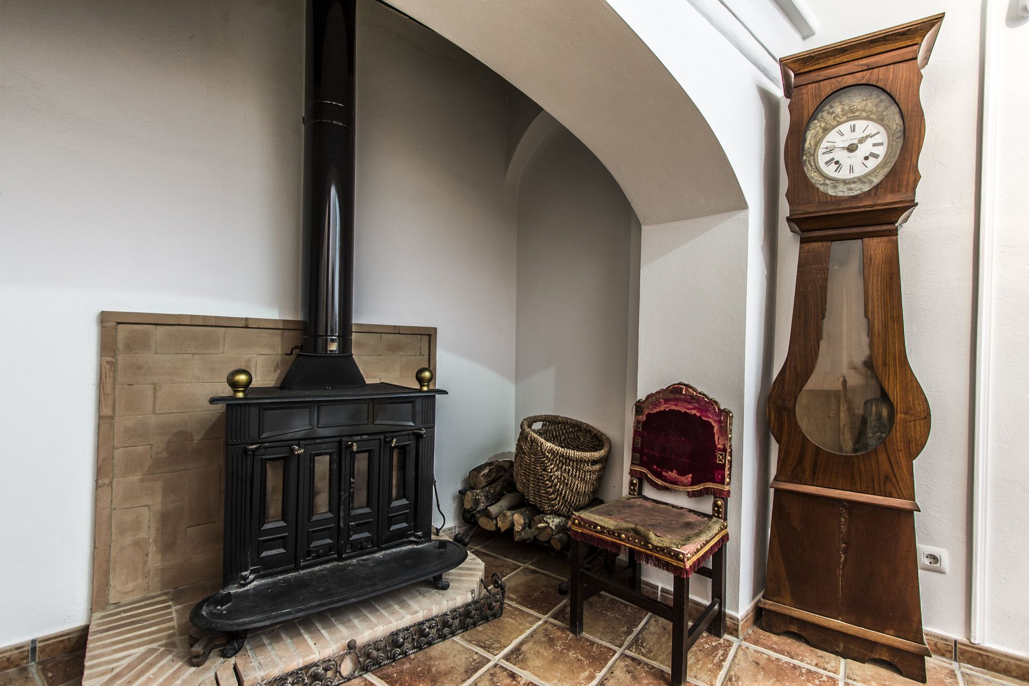 A room with a black wood-burning stove, a wooden grandfather clock, and a woven basket.