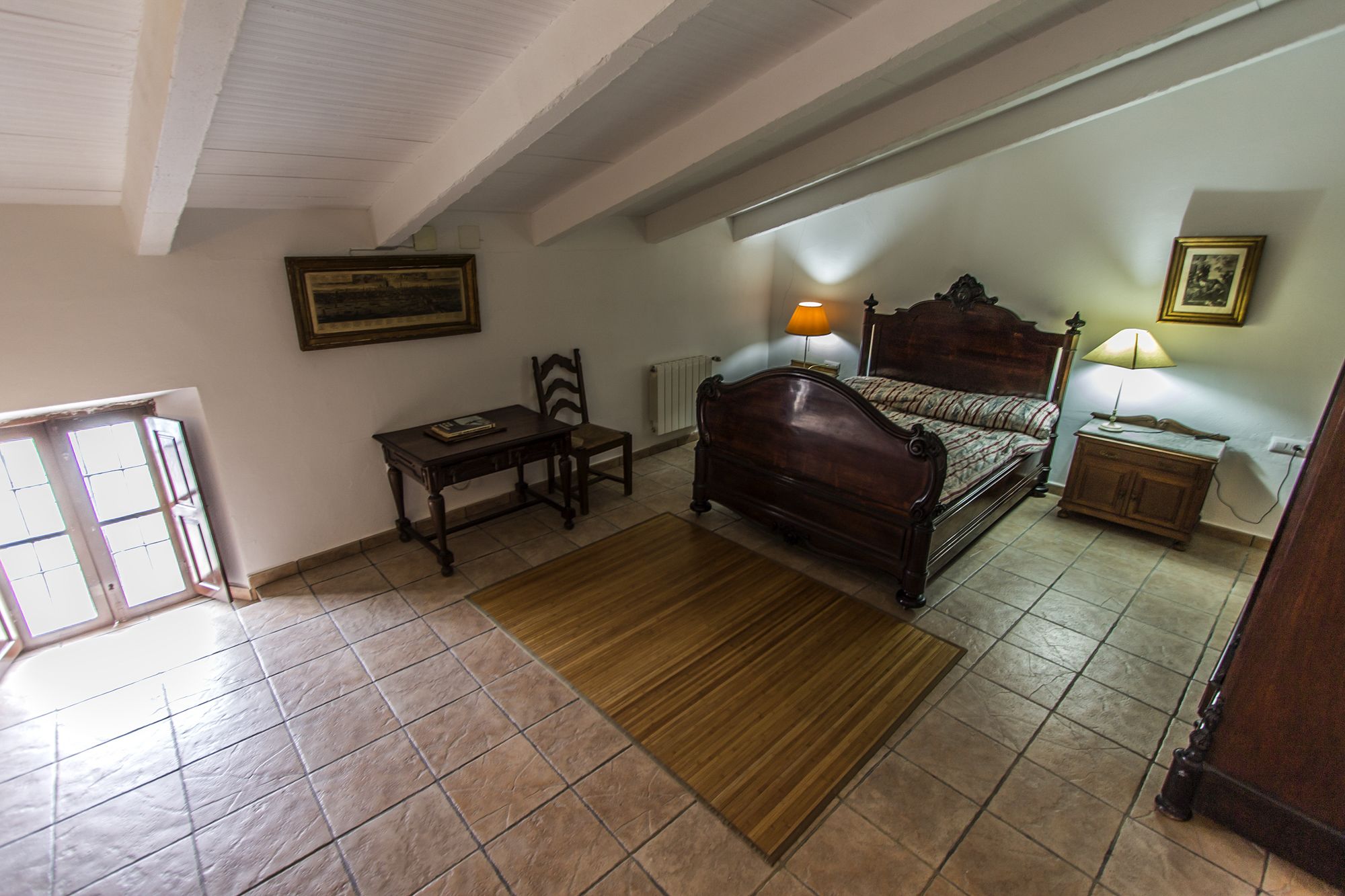 Un dormitorio con cama de madera, mesita de noche, silla, escritorio y radiador.