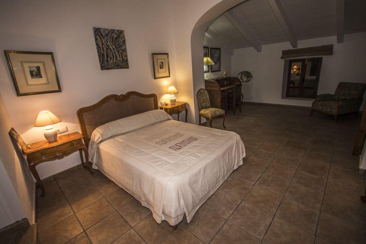 Ein Schlafzimmer mit einem Bett, zwei Nachttischen, einem Schreibtisch, einem Sessel und einem kleinen Tisch mit einer Lampe.