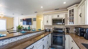 A modern kitchen with white cabinetry, granite countertops, stainless steel appliances, and a flat-screen TV. - Brand New Key Largo Home (Key Largo)