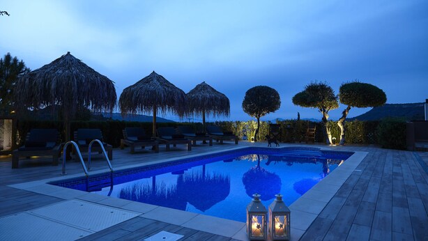Una piscina con sillones de descanso y sombrillas, rodeada de árboles y una terraza de madera.