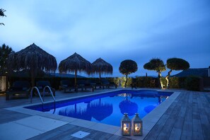 Une piscine entourée d’arbres et dotée d’une terrasse en bois, avec des chaises longues et des parasols.