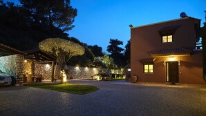 Un edificio bien iluminado con fachada de piedra, camino de grava y un árbol en primer plano.