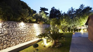 Un muro de piedra con un jardín bien cuidado, con una palmera y un árbol pequeño.