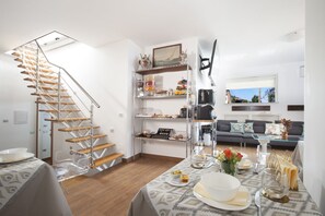 Eine moderne Küche mit einer Holztreppe, einem Essbereich mit Tisch für vier Personen und einem Wohnzimmer mit Sofa und Fenster.