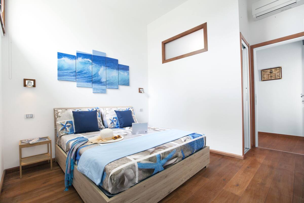 A bedroom with a bed, a nightstand, and a wall-mounted artwork.
