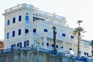 A multi-story building with balconies, a palm tree, and a stone wall.
