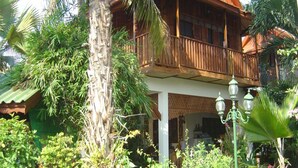 A wooden building with a balcony, surrounded by tropical vegetation. - Golden Teak Home Resort (Chiang Mai)