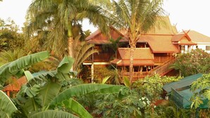 A traditional wooden house surrounded by lush tropical vegetation, including large banana leaves and palm trees. - Golden Teak Home Resort (Chiang Mai)