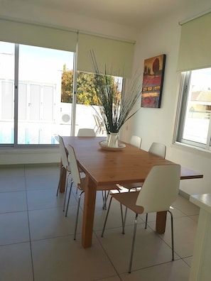 Un comedor moderno con una mesa de madera, sillas blancas y un jarrón con plantas altas.
