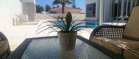 A glass-top table with a potted plant in the center, surrounded by wicker furniture.