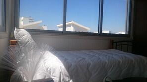 A bed with a white mattress and pillows, a window with a view of buildings, and a wooden headboard. - Colonial Beach Villa (Pervolia)