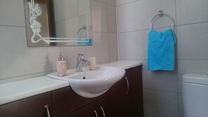 A bathroom with a white sink, two soap dispensers, a mirror, and a blue towel hanging on a metal ring. - Colonial Beach Villa (Pervolia)