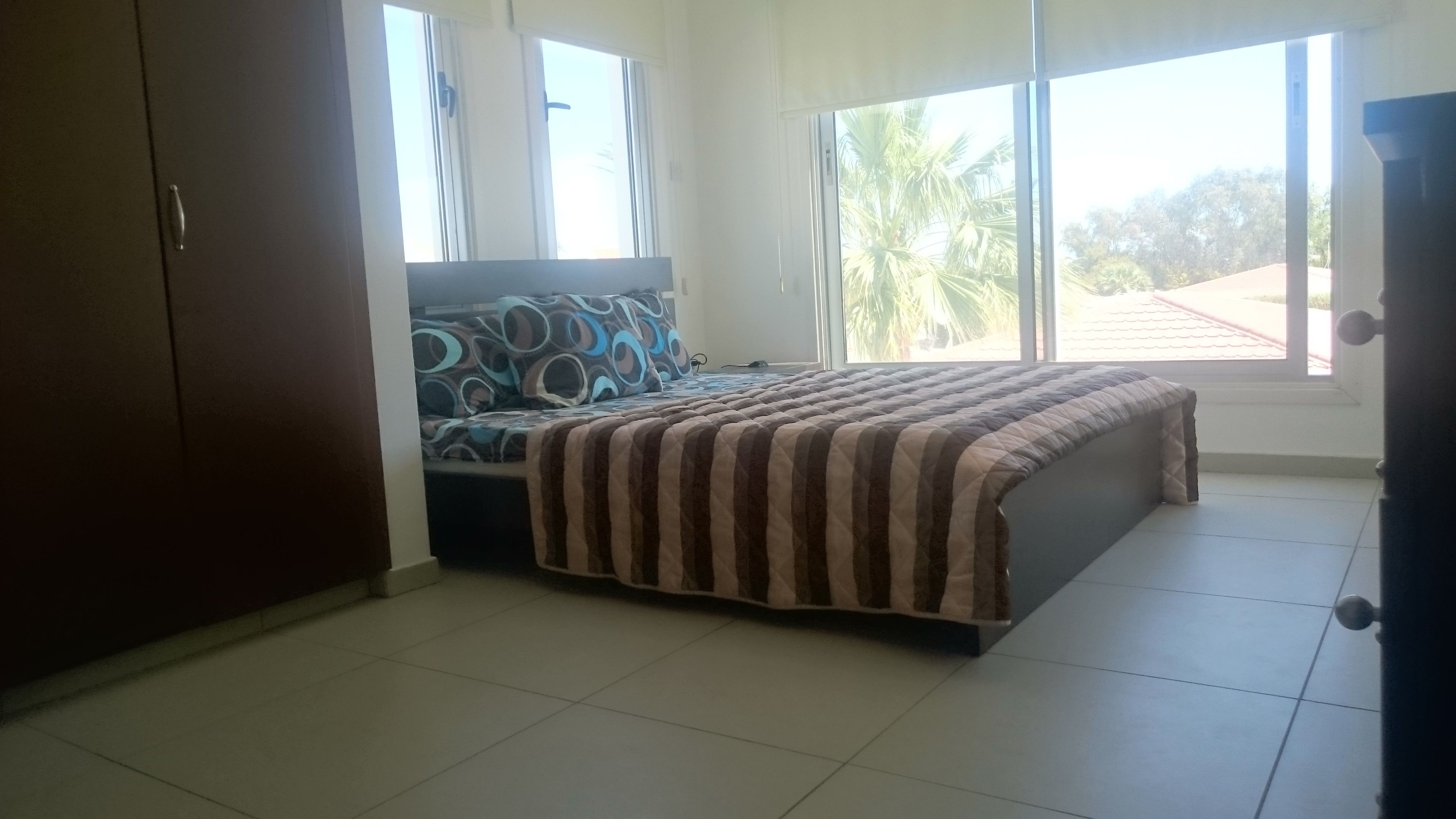 A bedroom with a bed, a wardrobe, and large windows.