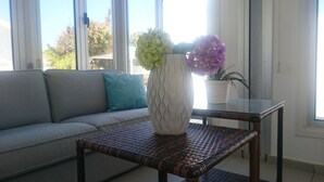 Ein Wohnzimmer mit einer Couch, einem Glastisch mit Blumenvase und einem Topfpflanzen.