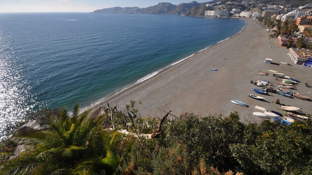Una playa costera con barcos, edificios y cielo despejado.