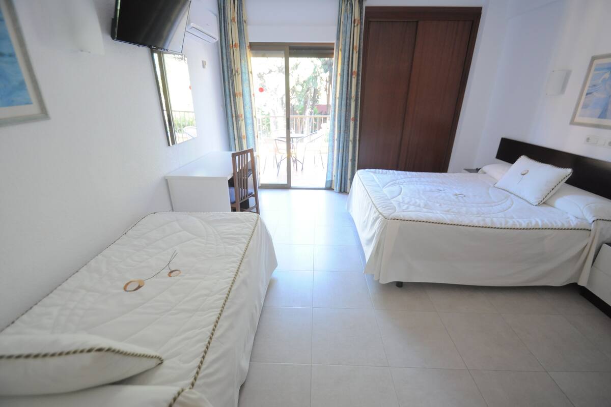 Habitación de hotel con dos camas, un televisor montado en la pared y un balcón con vistas al exterior.