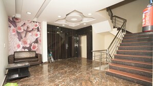 Un hall con suelo de mármol, un sofá, una escalera y un extintor.