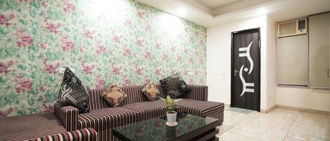 A living room with striped sofas, a glass coffee table, and a floral wallpaper.