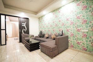 A living room with striped sofas, a coffee table, and a floral wallpaper. - Kabul Hotel Medanta Hospital, Gurugram (Gurugram)