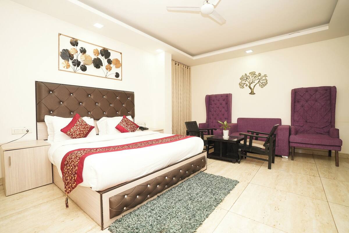A hotel room with a large bed, two armchairs, a small table, and a ceiling fan.