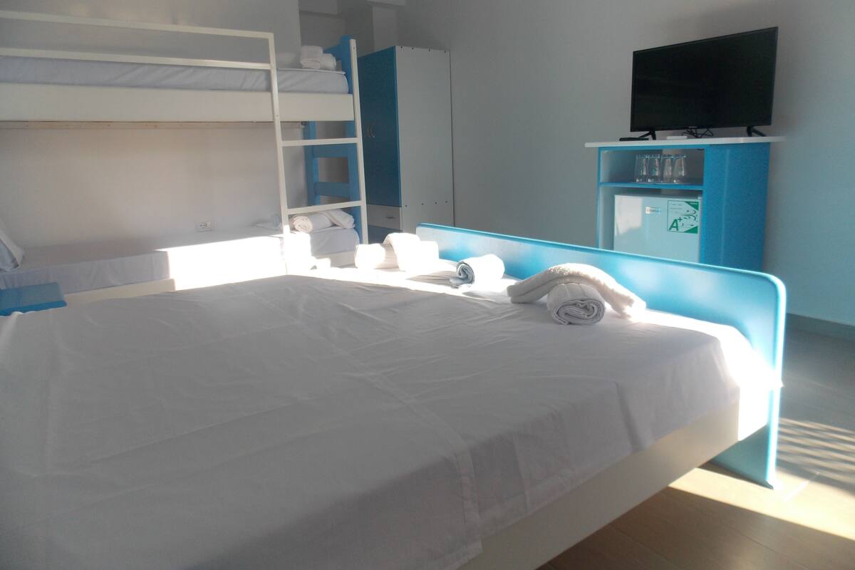 A hotel room with a bunk bed, a flat bed, a TV, and a minibar.