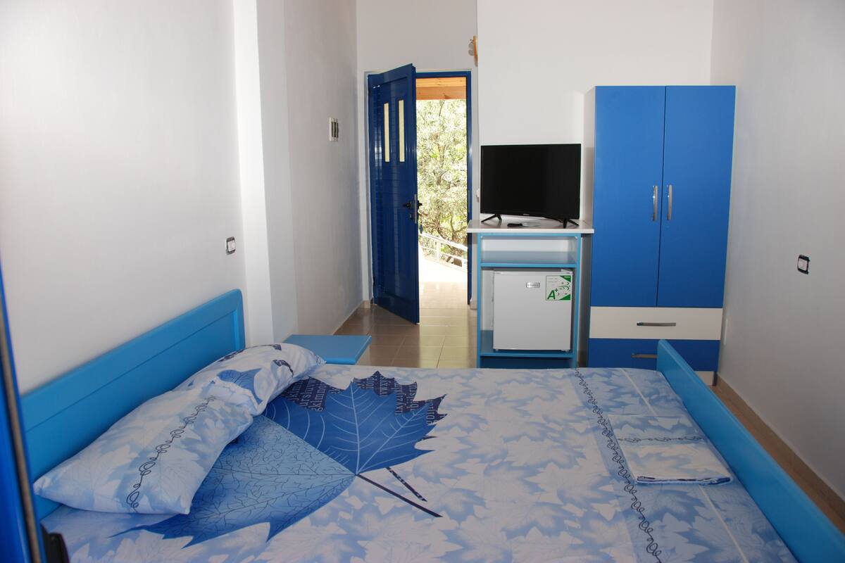 A bedroom with a bed, a wardrobe, a desk, and a television.