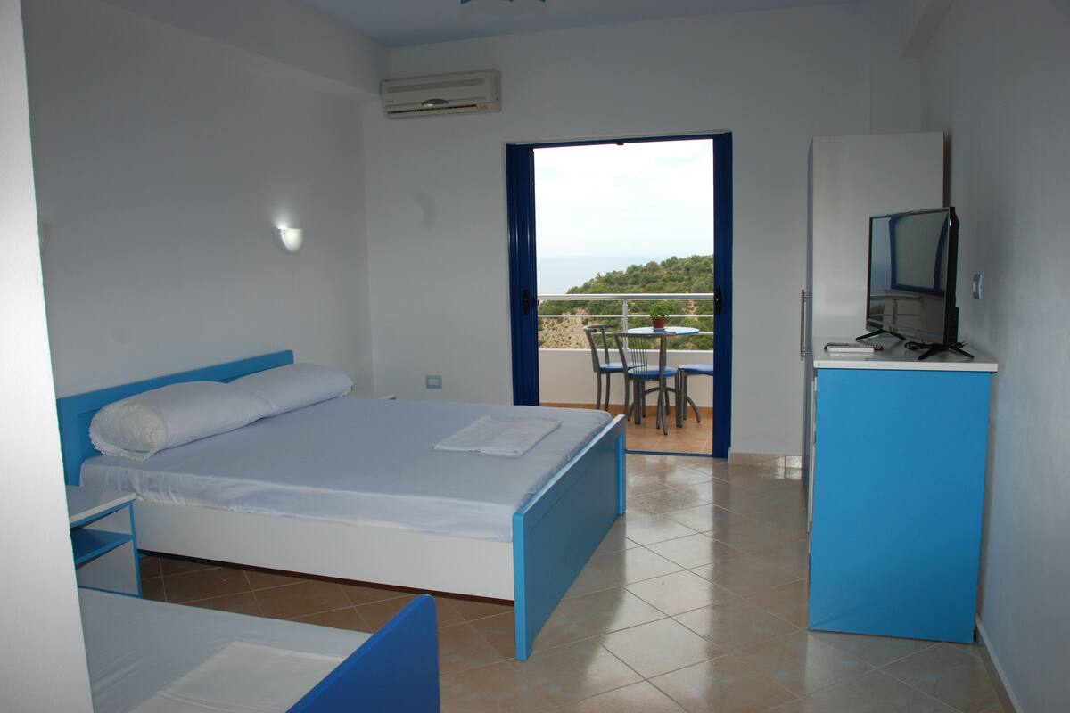A bedroom with a bed, a desk, and a small kitchenette.