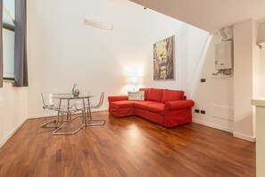 A modern living room with a red sectional sofa, a glass dining table with chairs, and a wall-mounted light fixture.