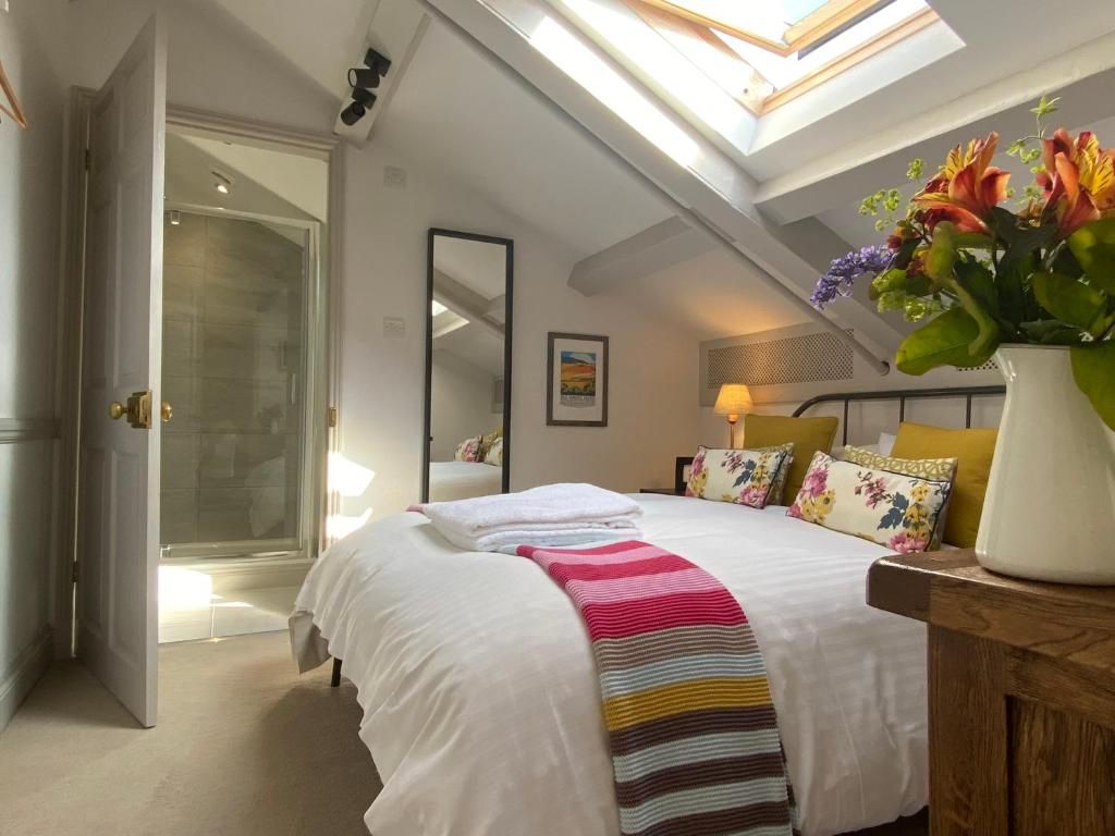 A bedroom with a skylight, a bed with a striped blanket, a bedside table with a vase of flowers, and a shower area.
