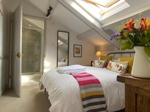A bedroom with a skylight, a bed with a striped blanket, a bedside table with a vase of flowers, and a shower area. - Pardlestone Farm: B&B (Bridgwater)
