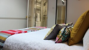 Una cama bien hecha con una manta a rayas, varios almohadones y un espejo en la pared.