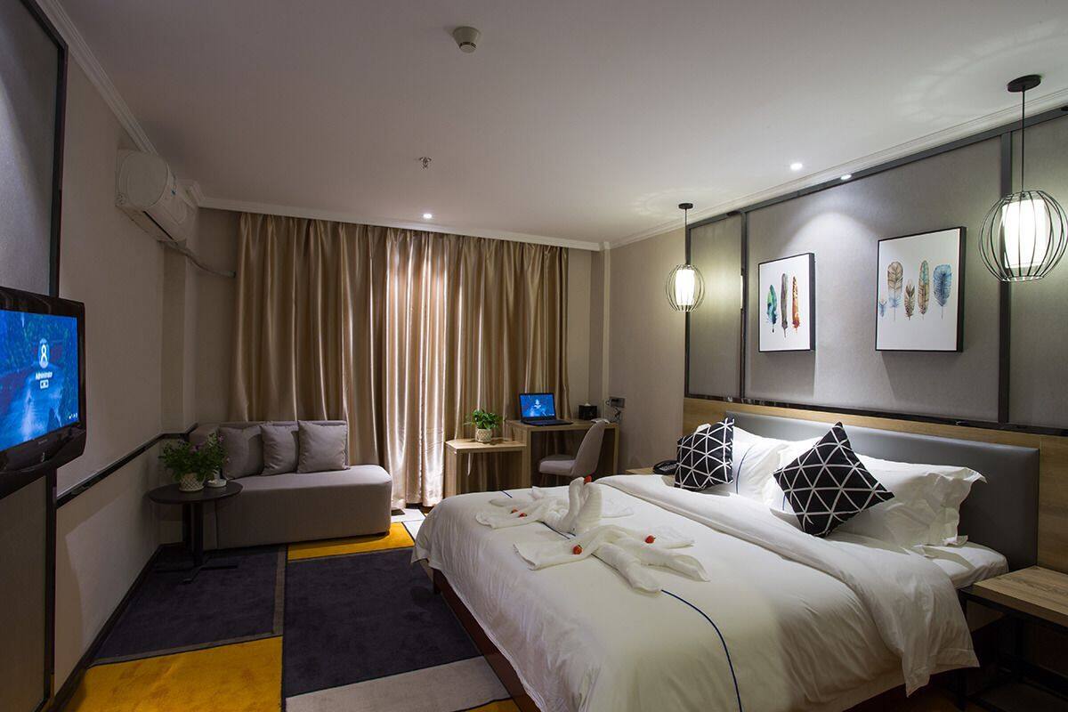 A modern hotel room with a large bed, a desk with a computer, a TV, and artwork on the wall.