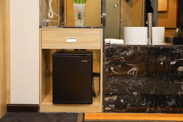 A compact minibar with a black refrigerator, a wooden drawer unit, and a marble countertop with a sink and two white cups. - Homies Hotel (Guangzhou)
