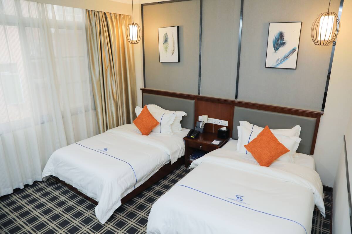 A hotel room with two beds, a nightstand, a telephone, and artwork on the walls.
