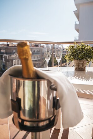 Une bouteille de champagne dans un récipient métallique sur un balcon, avec deux verres et une plante en pot.
