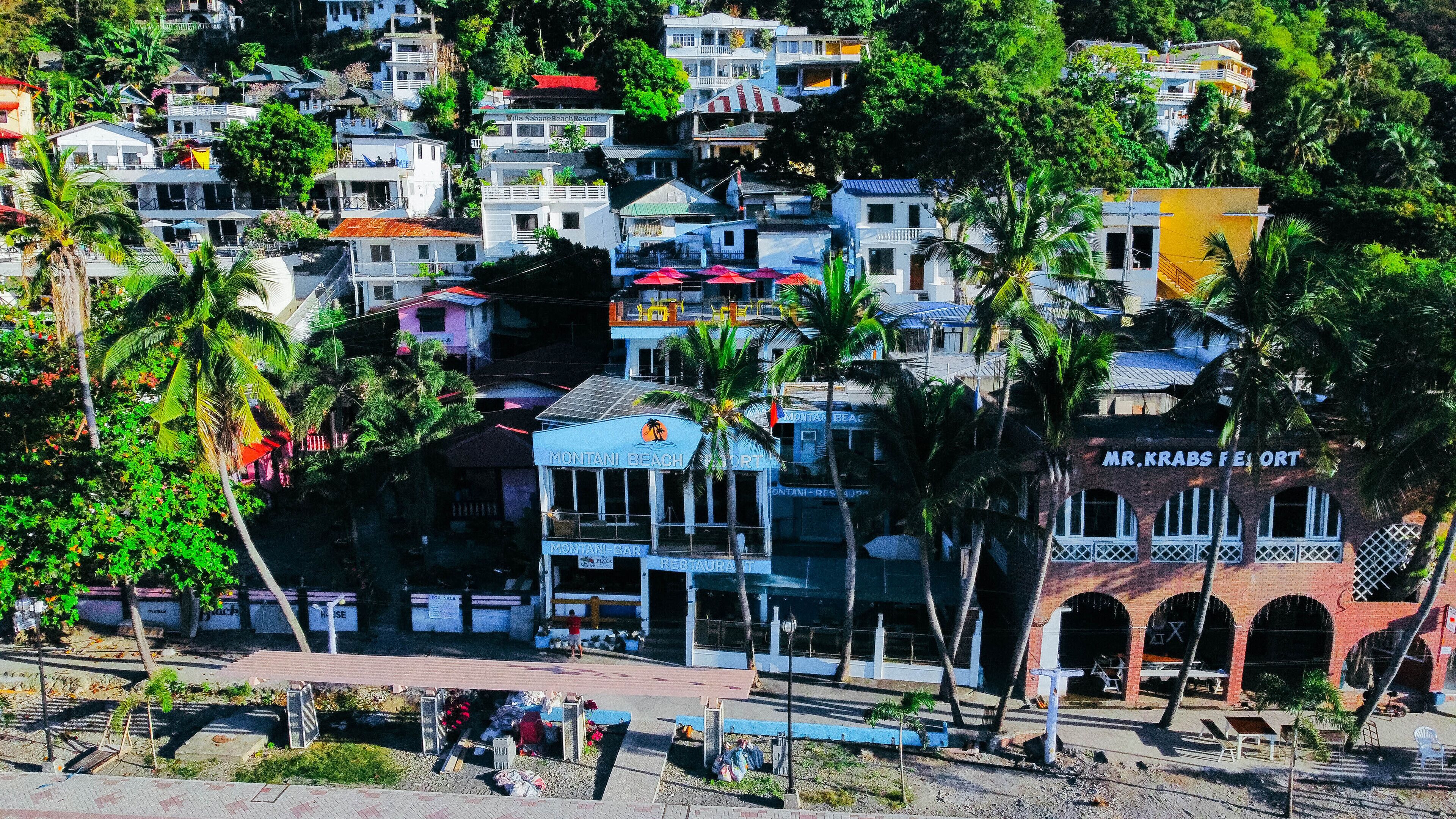 Un complejo turístico frente al mar con varias edificaciones, incluyendo un bar y restaurante, y un letrero llamativo que dice Mr. Krabs Resort.