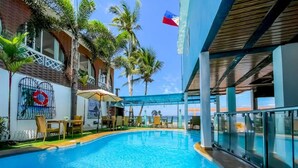 A swimming pool with a view of the beach, surrounded by palm trees and a flag. - Montani Beach Resort Puerto Galera powered by Cocotel (Puerto Galera)