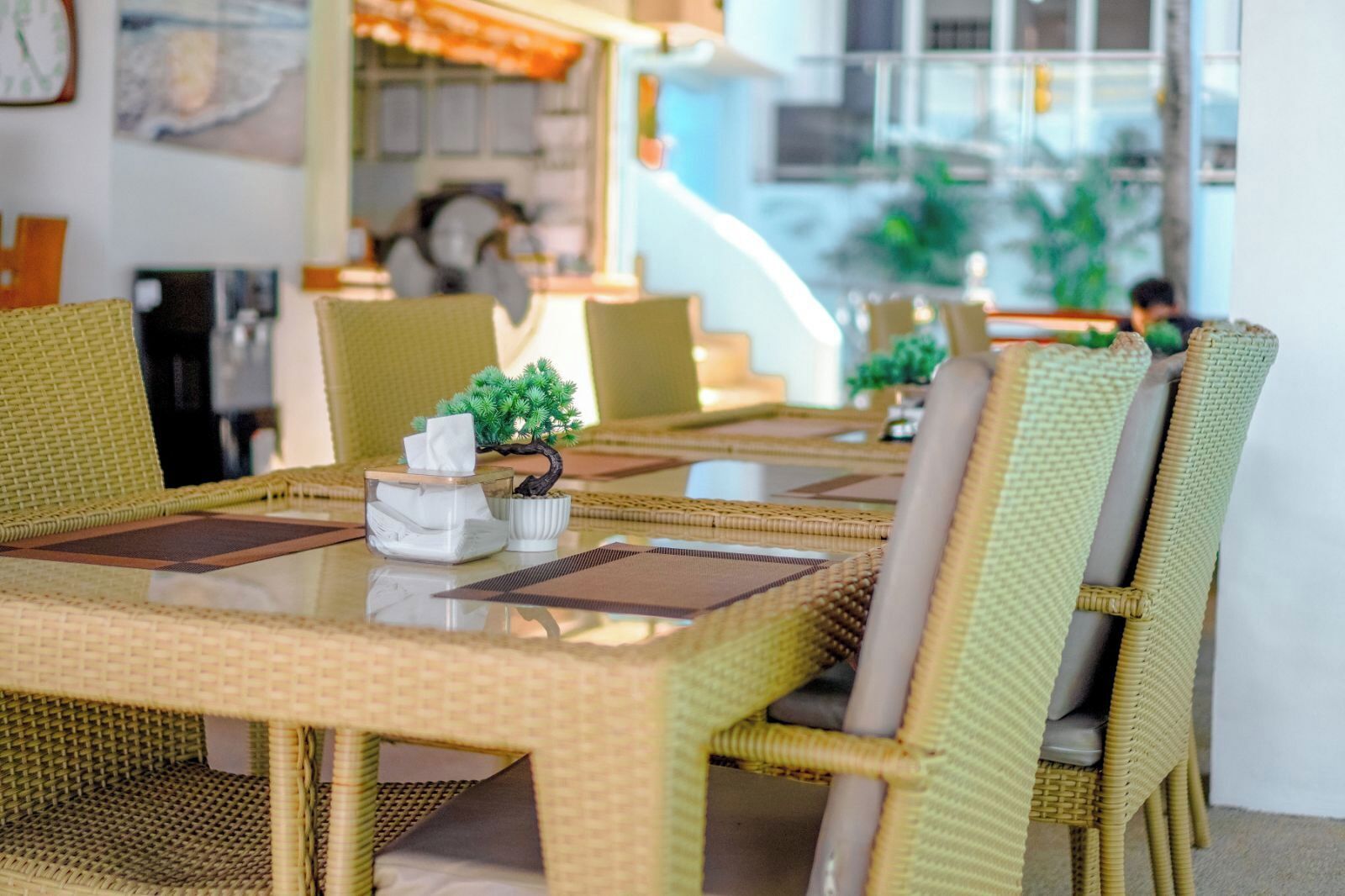 A dining area with wicker furniture, a small bonsai tree, and a tissue box on the table.