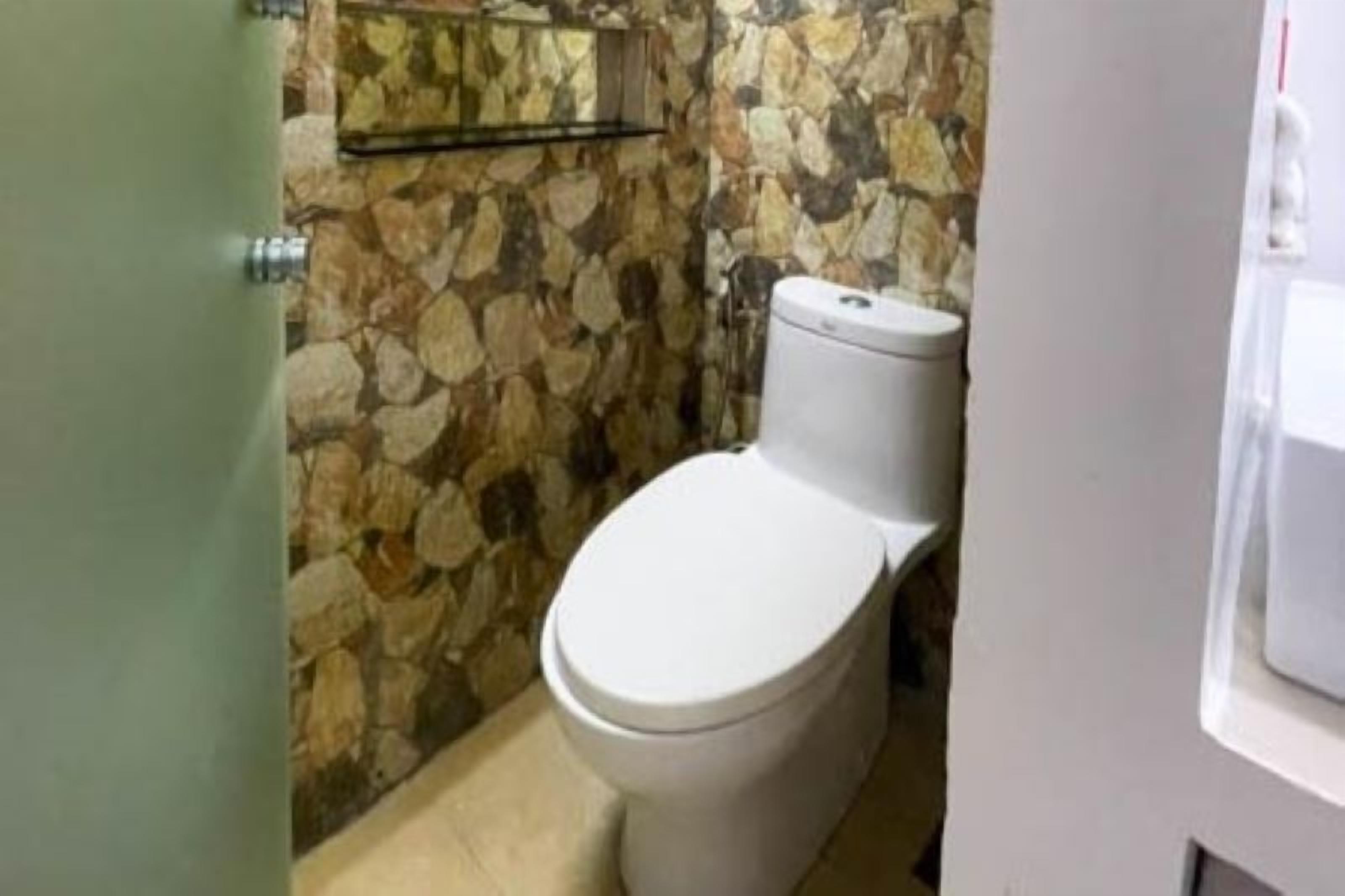 A bathroom with a stone wall, a toilet, and a glass shelf.