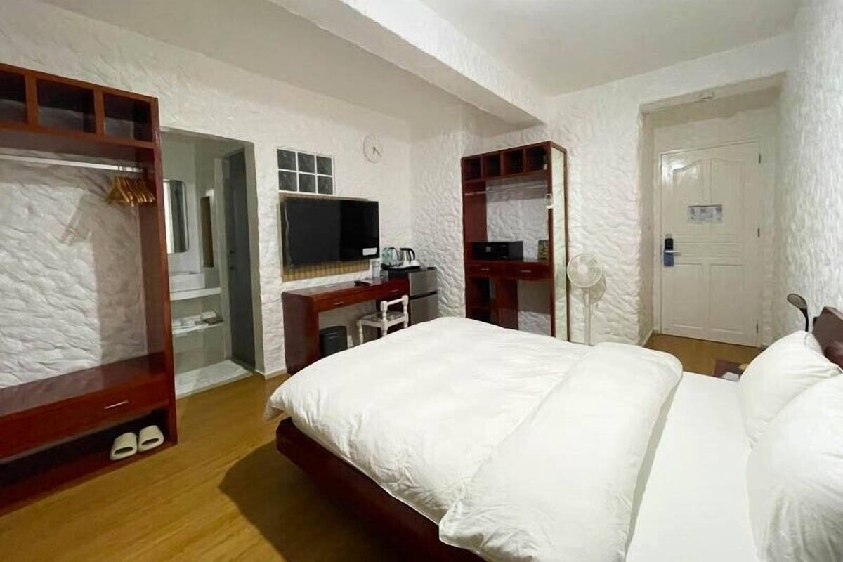 Un dormitorio con una cama grande, un escritorio con silla, un televisor y un armario.