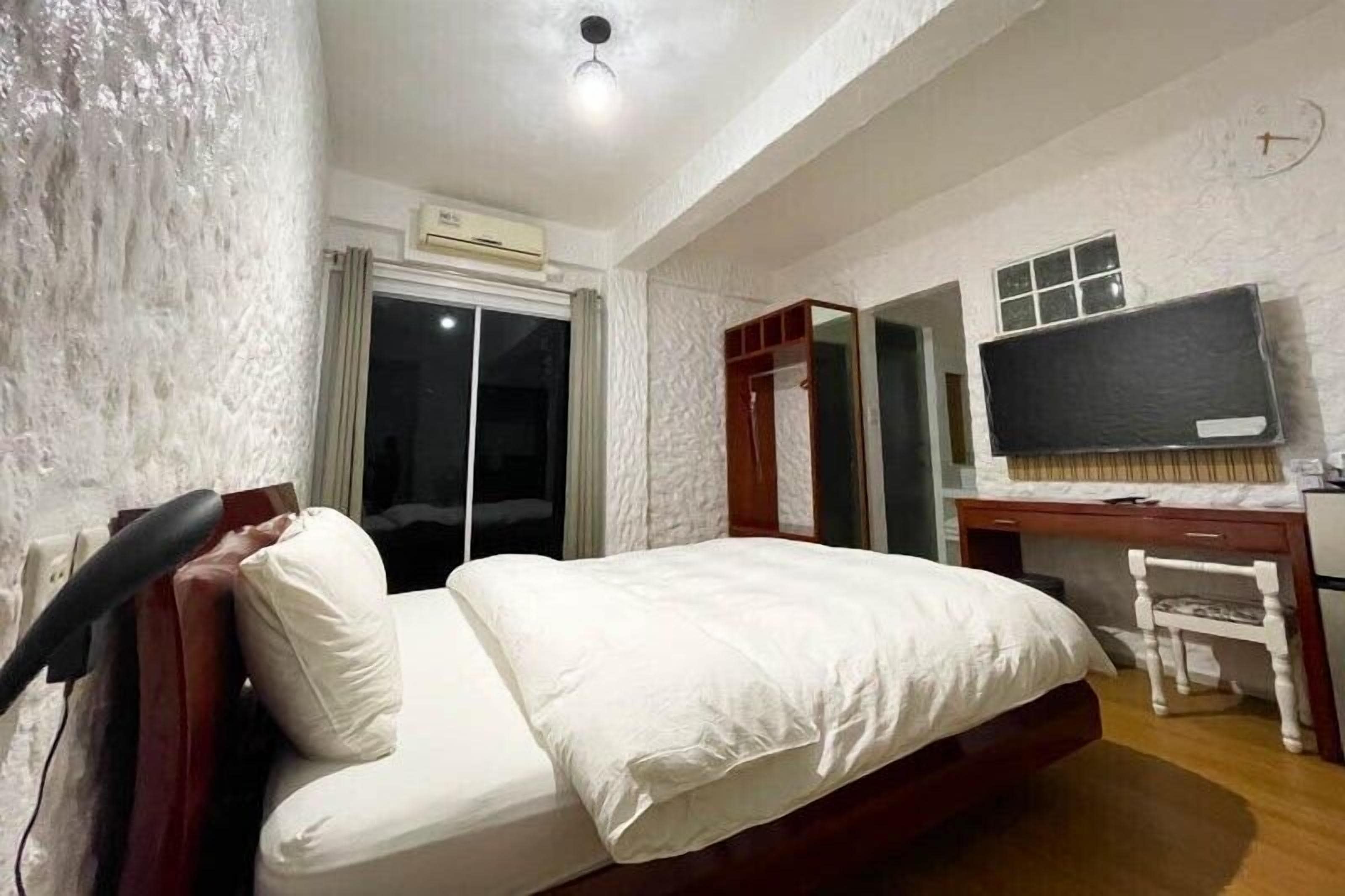 A hotel room with a bed, a desk with a chair, a television, and a wardrobe.