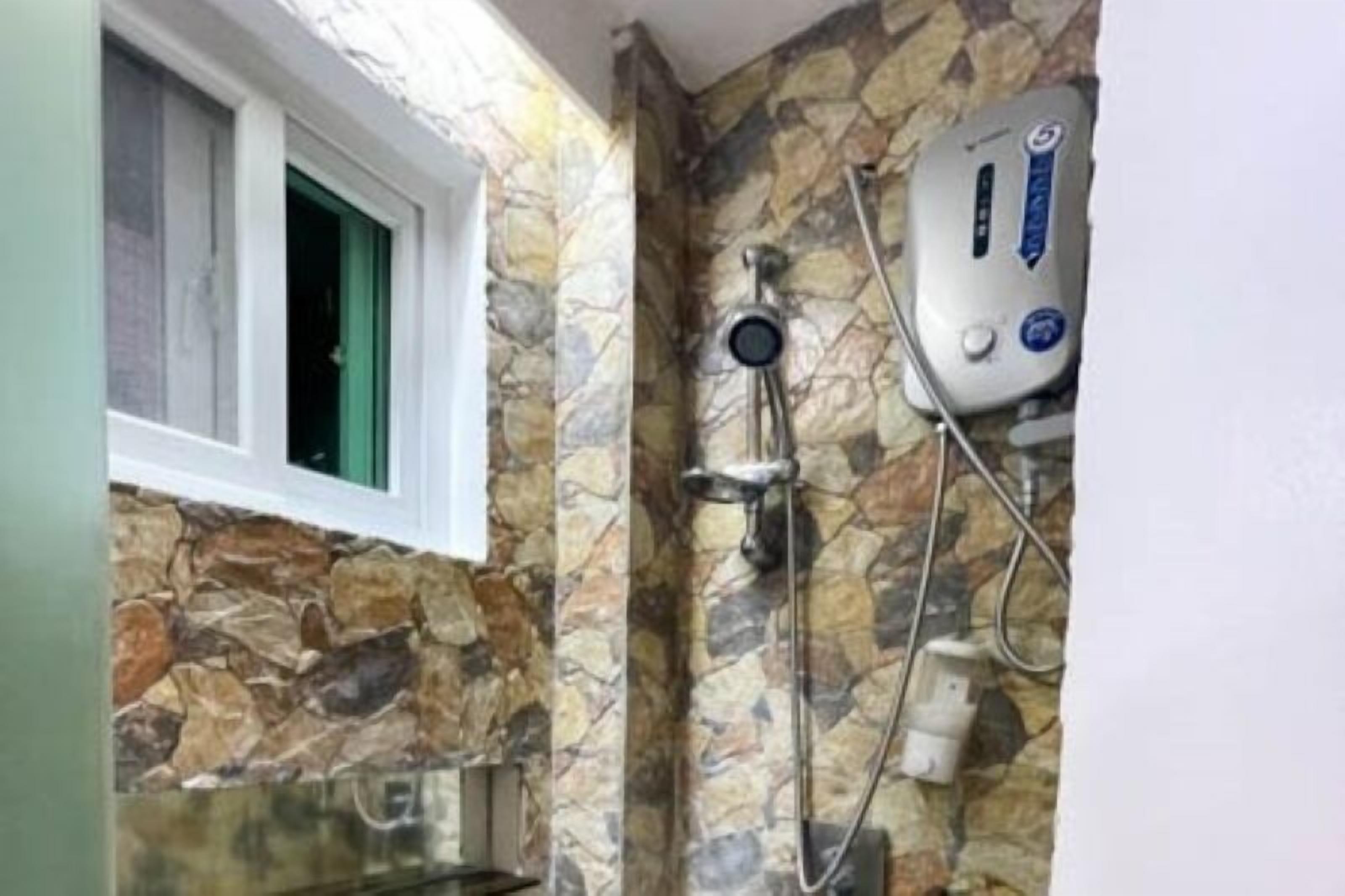 A bathroom with a stone wall, a window with a green frame, and a shower unit with a control panel.